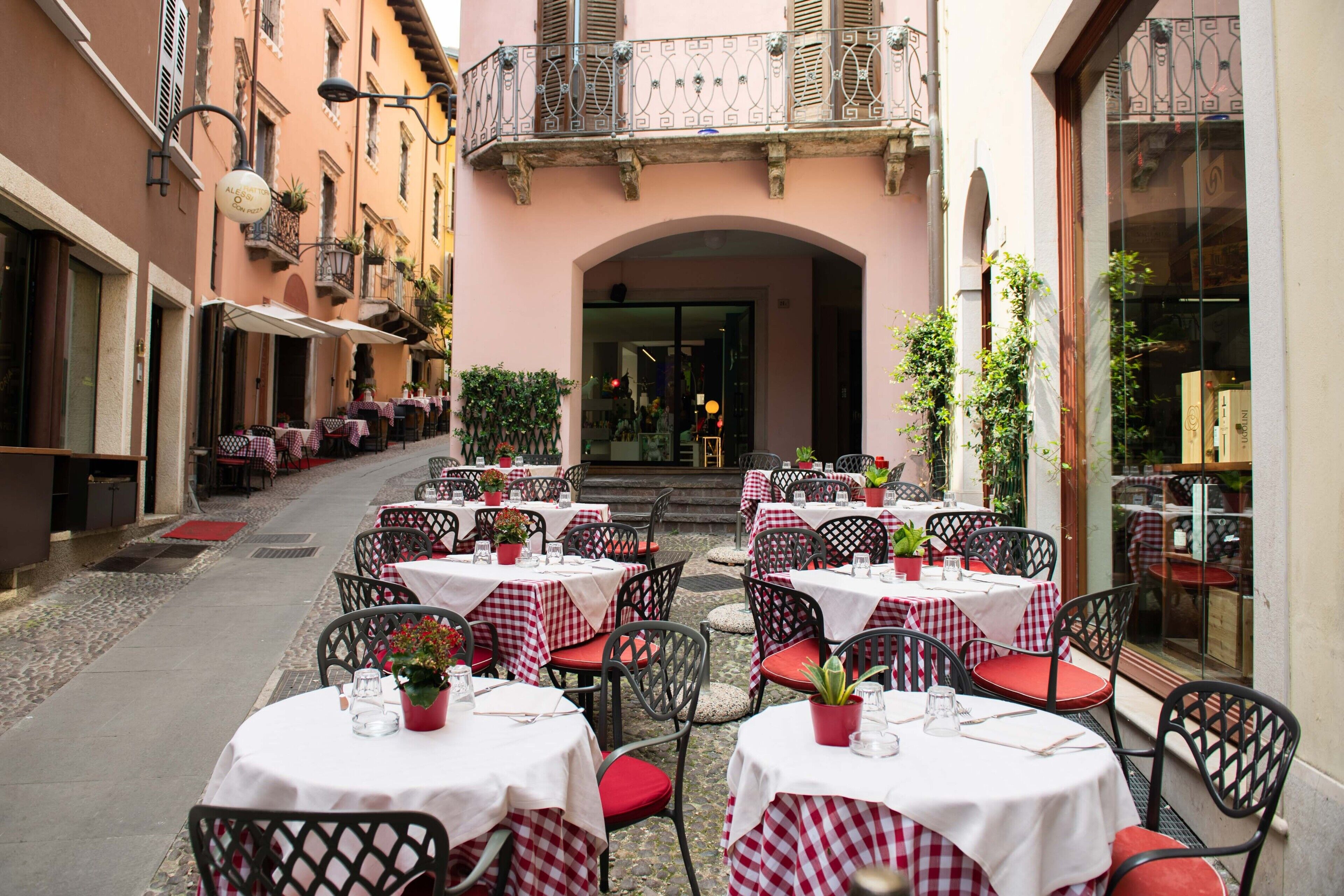 Un café en plein air avec des tables et des chaises, un chemin pavé et l’entrée d’un bâtiment.