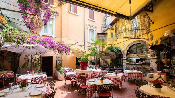 Un espace extérieur aménagé pour les repas, avec des tables et des chaises, entouré de plantes et de fleurs en pot.