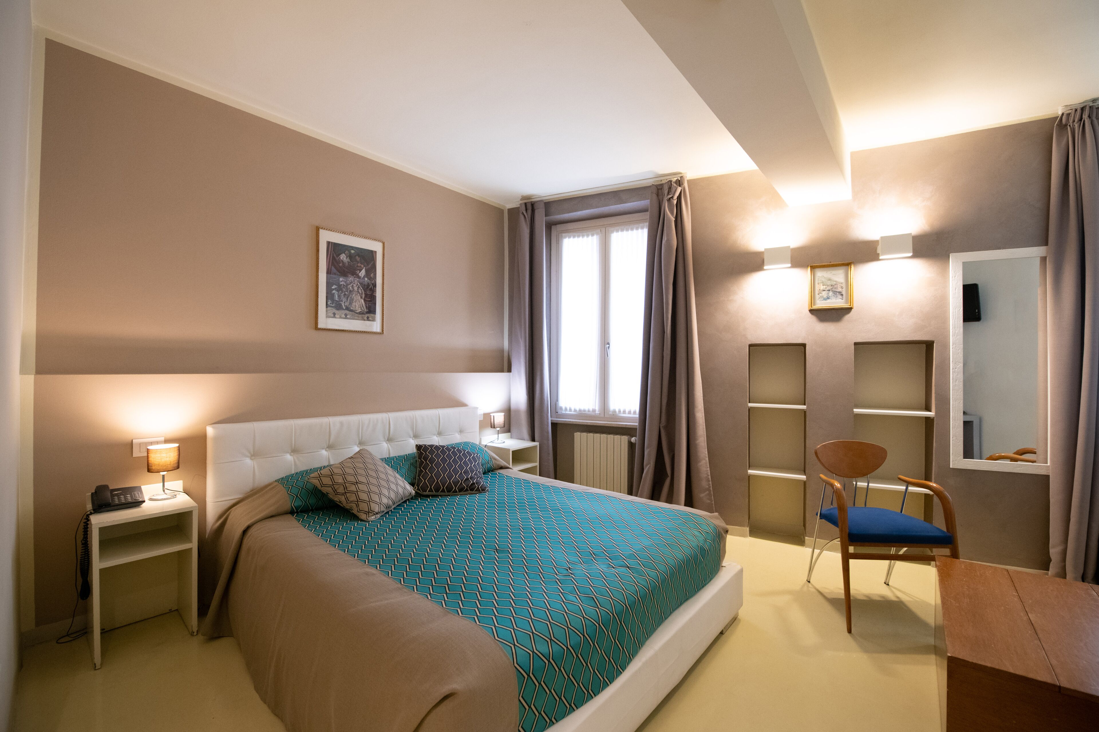 A bedroom with a bed, bedside tables, a chair, a desk, and a window with curtains.