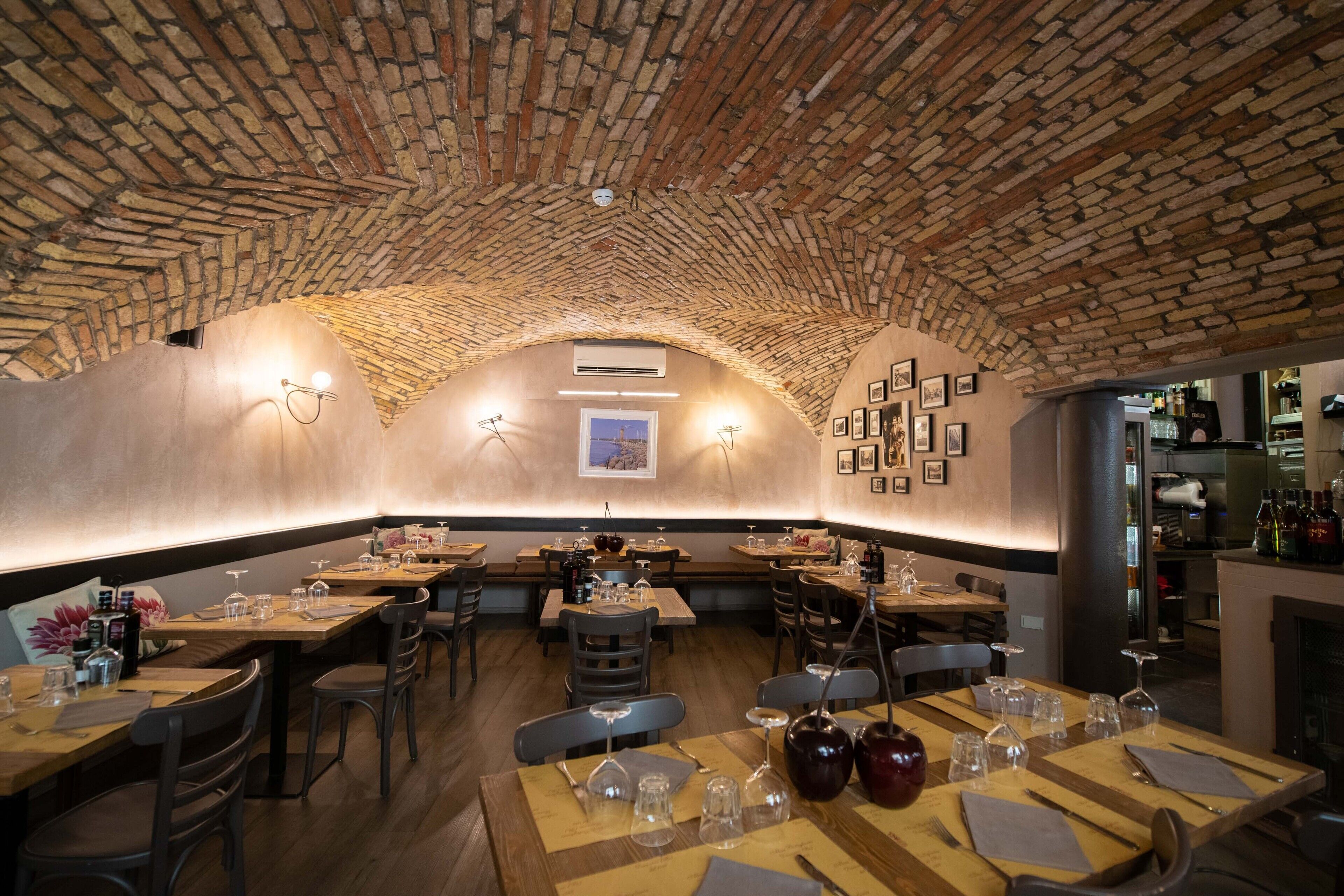 Un restaurant avec un plafond en briques, des tables et des chaises en bois, et un bar situé à l’arrière-plan.