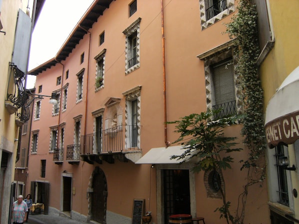 A narrow street with a building featuring multiple windows and balconies, a visible door, and a sign that reads "Café".