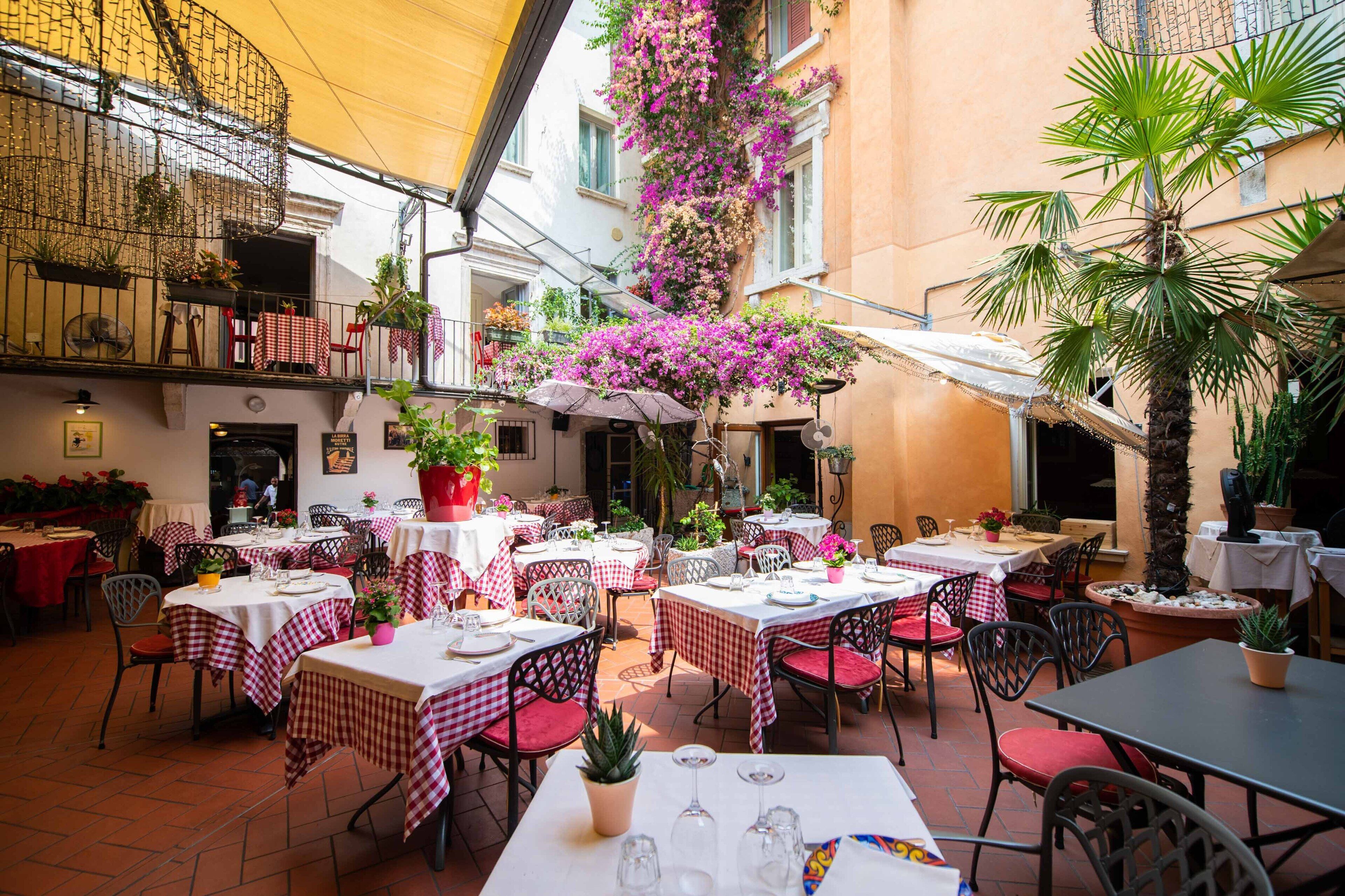An outdoor dining area with tables and chairs, surrounded by potted plants and flowers.
