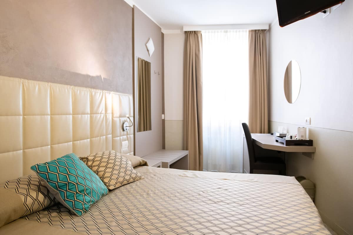 A hotel room with a large bed, a desk, a chair, a TV, and a window with curtains.