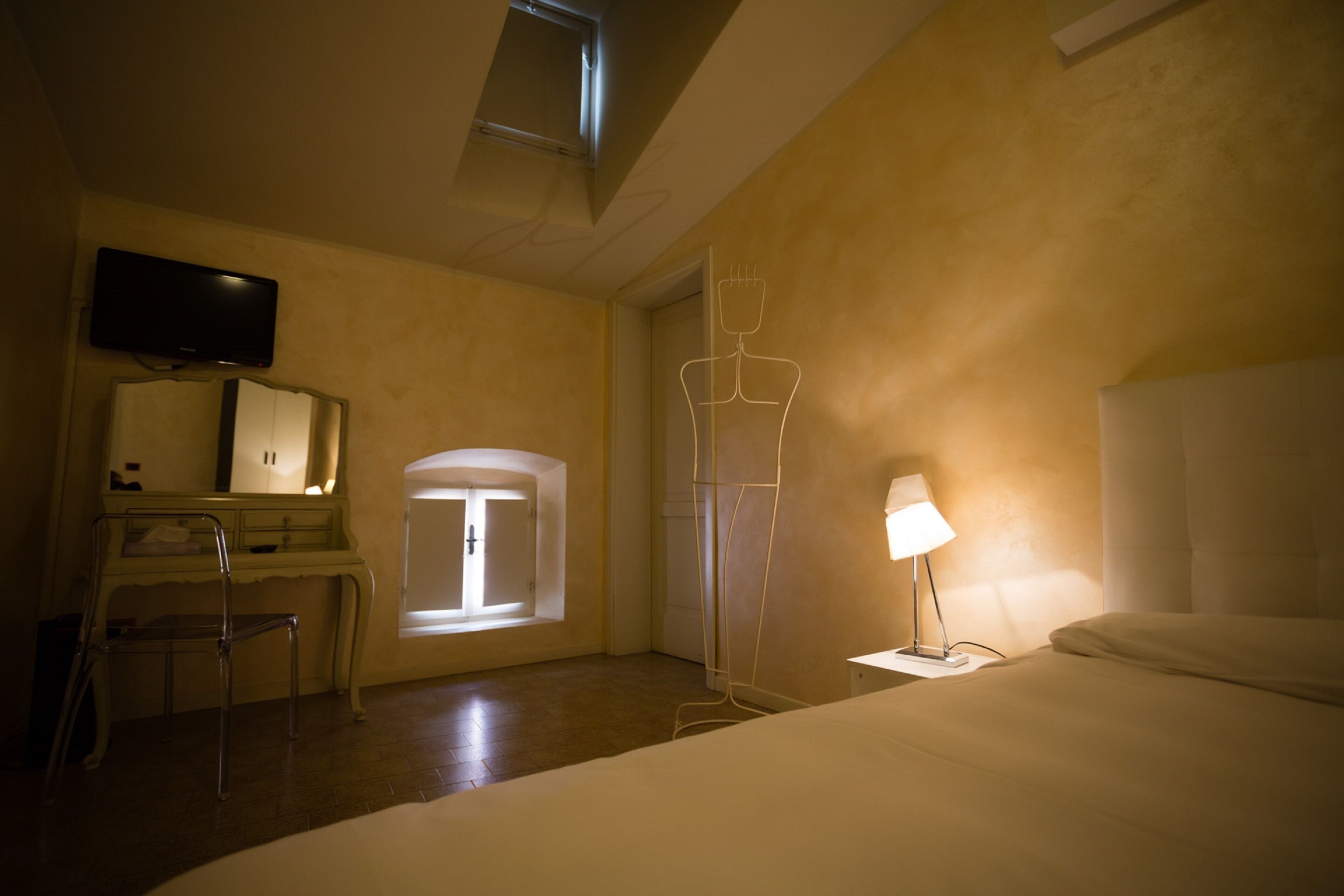 Una habitación de hotel con cama, escritorio con silla, televisor y lámpara de pie.