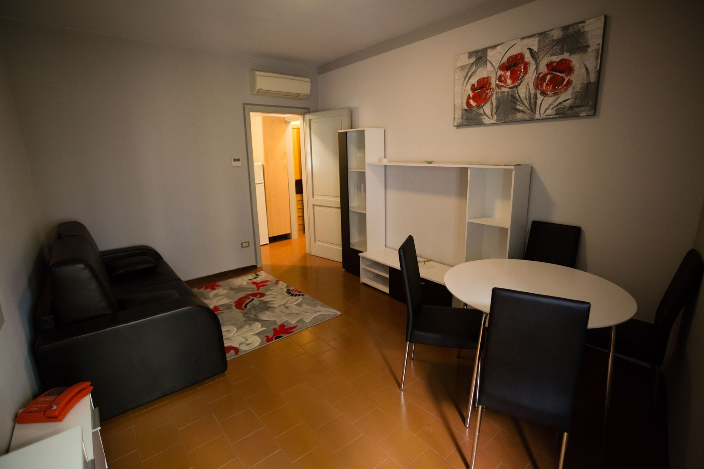 En kompakt opholdsstue med en sofa, et spisebord med stole, et lille køkken og en dør, der fører til et andet rum.