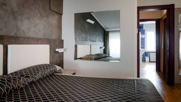 Una habitación de hotel moderna con una cama grande, cabecero integrado, mesita de noche pequeña y un espejo amplio.