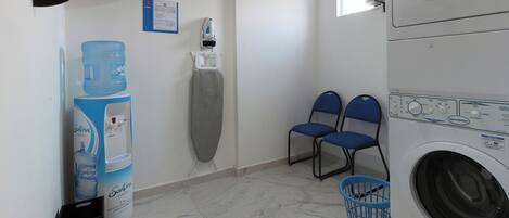 Un lavadero con lavadora, dos sillas, dispensador de agua y una máquina de agua grande.