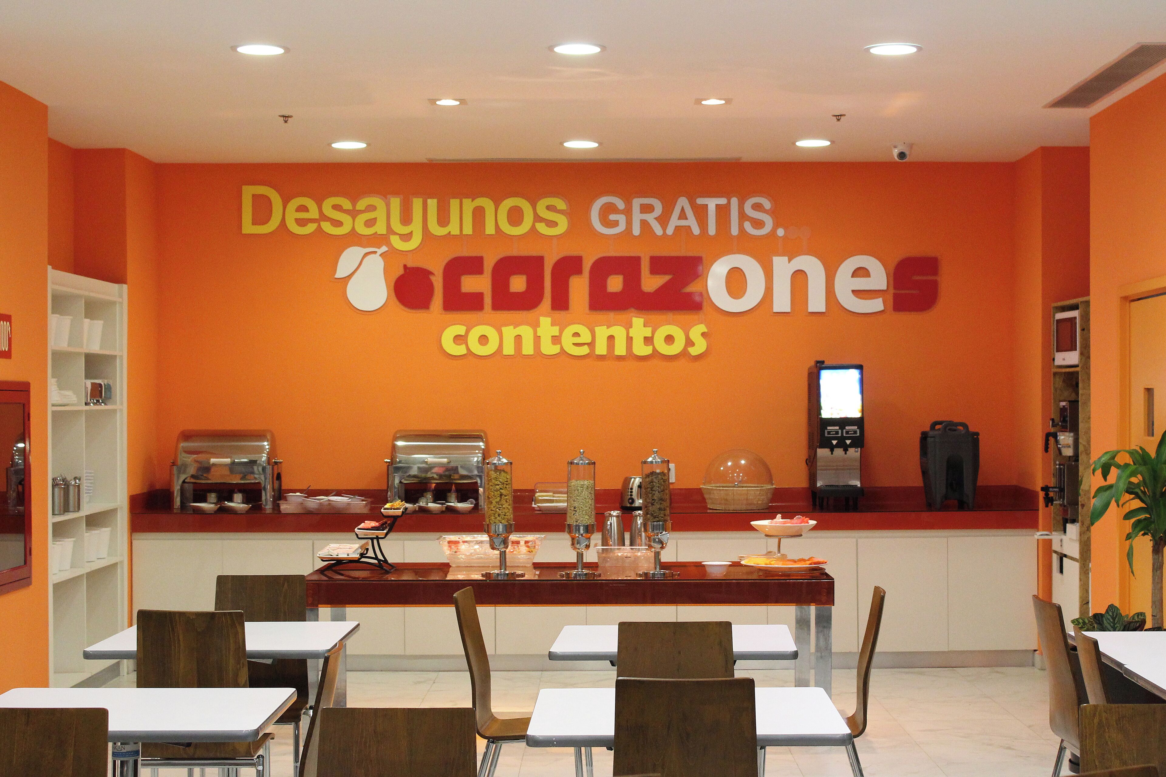 Una cafetería con paredes anaranjadas, mesas blancas y diversas opciones de comida.