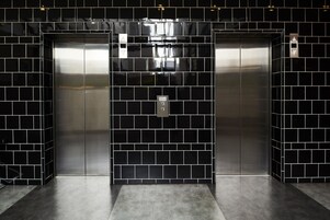 Un elevador moderno con paredes de azulejos negros y detalles metálicos.