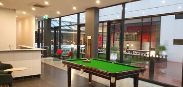 Una mesa de billar en un ambiente interior moderno con ventanas amplias y una zona de recepción.