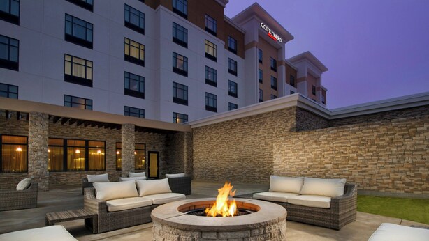 A courtyard with a stone fire pit surrounded by wicker furniture and a stone wall. - Courtyard by Marriott Dallas DFW Airport North/Grapevine (Grapevine)
