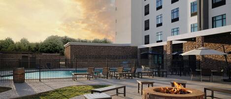 A hotel courtyard with a swimming pool, outdoor seating, and a fire pit.
