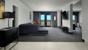 A modern hotel room with a grey sofa, a small table, a flat-screen TV mounted on the wall, and a balcony with a view of the sky. - Courtyard by Marriott Dallas DFW Airport North/Grapevine (Grapevine)