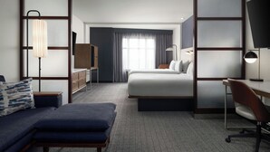 A hotel room with a bed, a desk, a chair, a sofa, a lamp, and a TV. - Courtyard by Marriott Dallas DFW Airport North/Grapevine (Grapevine)