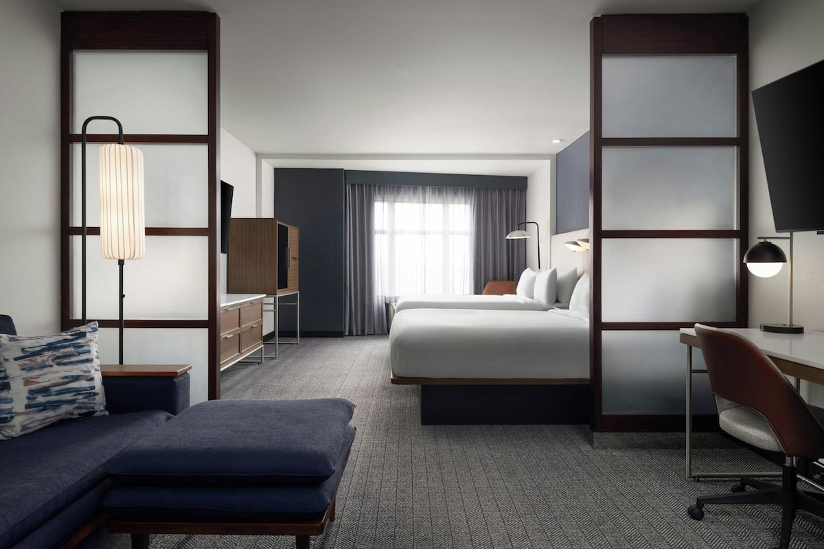 A hotel room with a bed, a desk, a chair, a sofa, a lamp, and a TV.