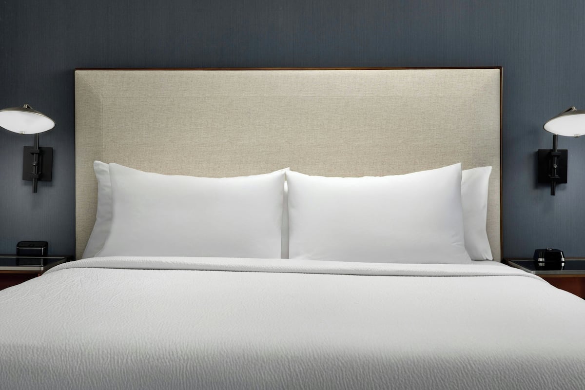 A neatly made bed with white linens and a headboard, flanked by two wall-mounted lamps.