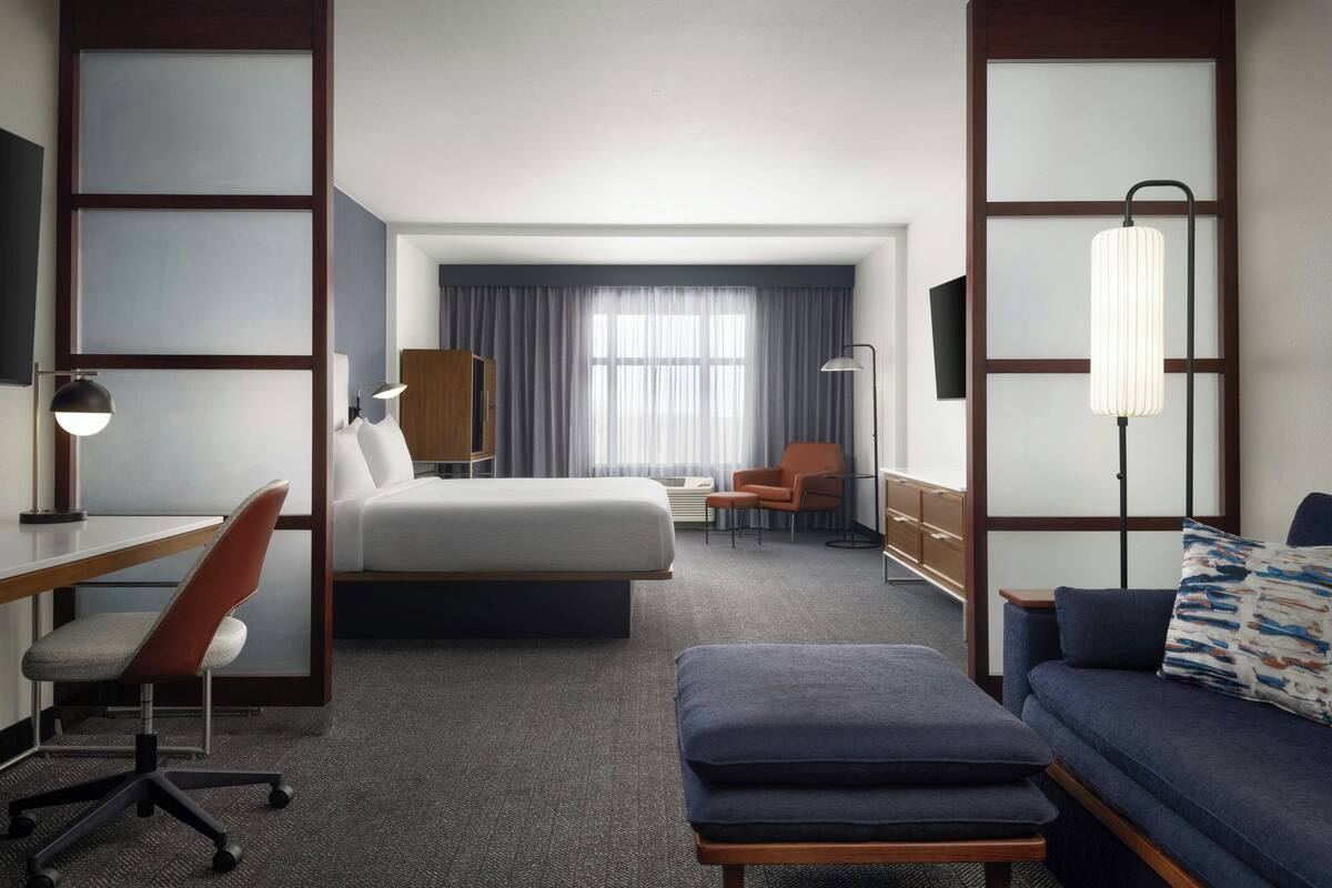 A hotel room with a bed, a desk with a chair, a sofa, a lamp, and a TV.