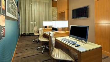 A hotel room with a desk, two chairs, a computer, and a TV.