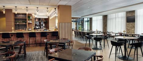 Un moderno vestíbulo de hotel con zona de bar, mesas y sillas para comer.