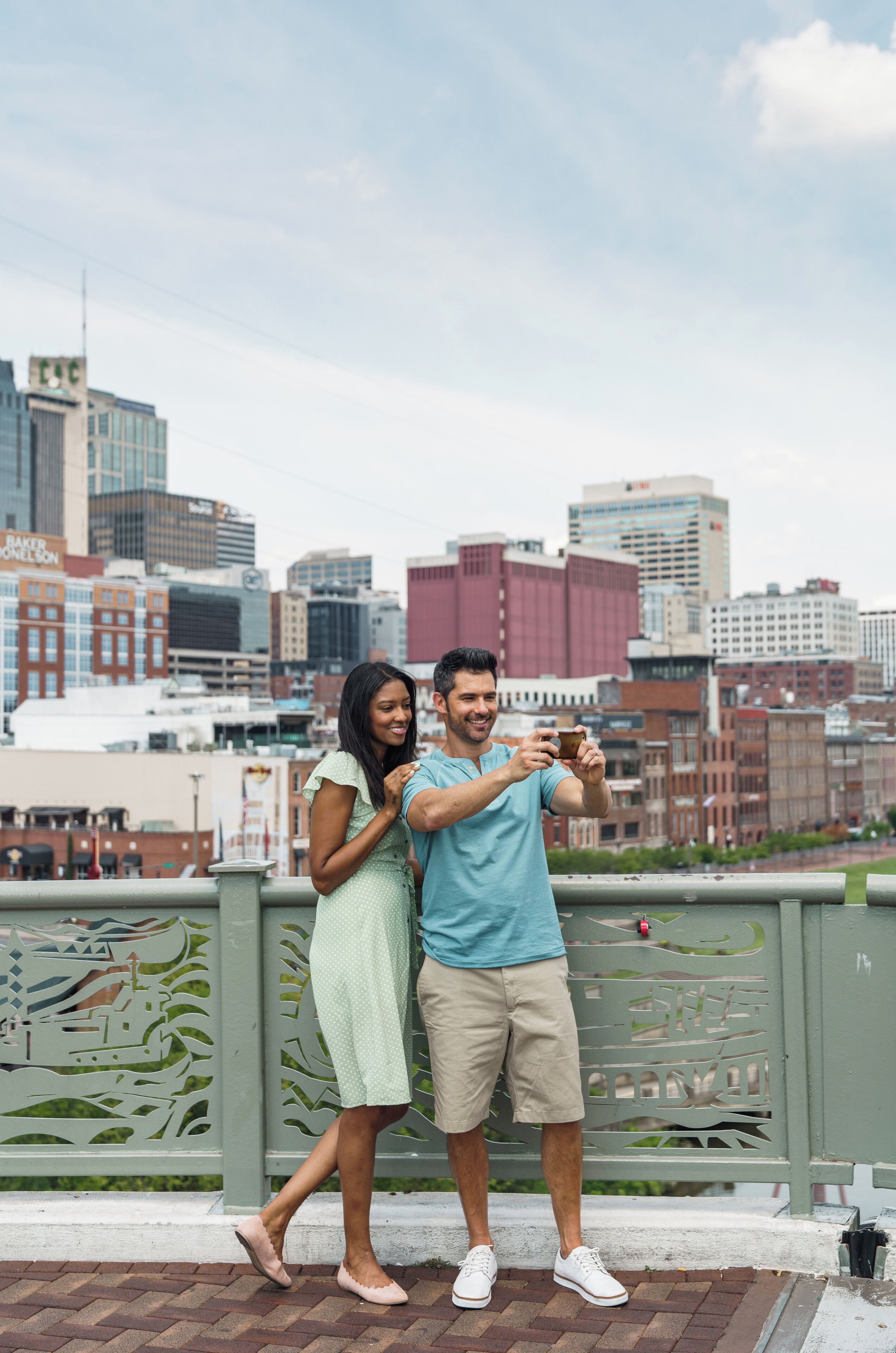 Una pareja tomándose un selfie en un balcón con un horizonte urbano de fondo.