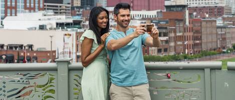 Una pareja tomándose un selfie en un balcón con un horizonte urbano de fondo.