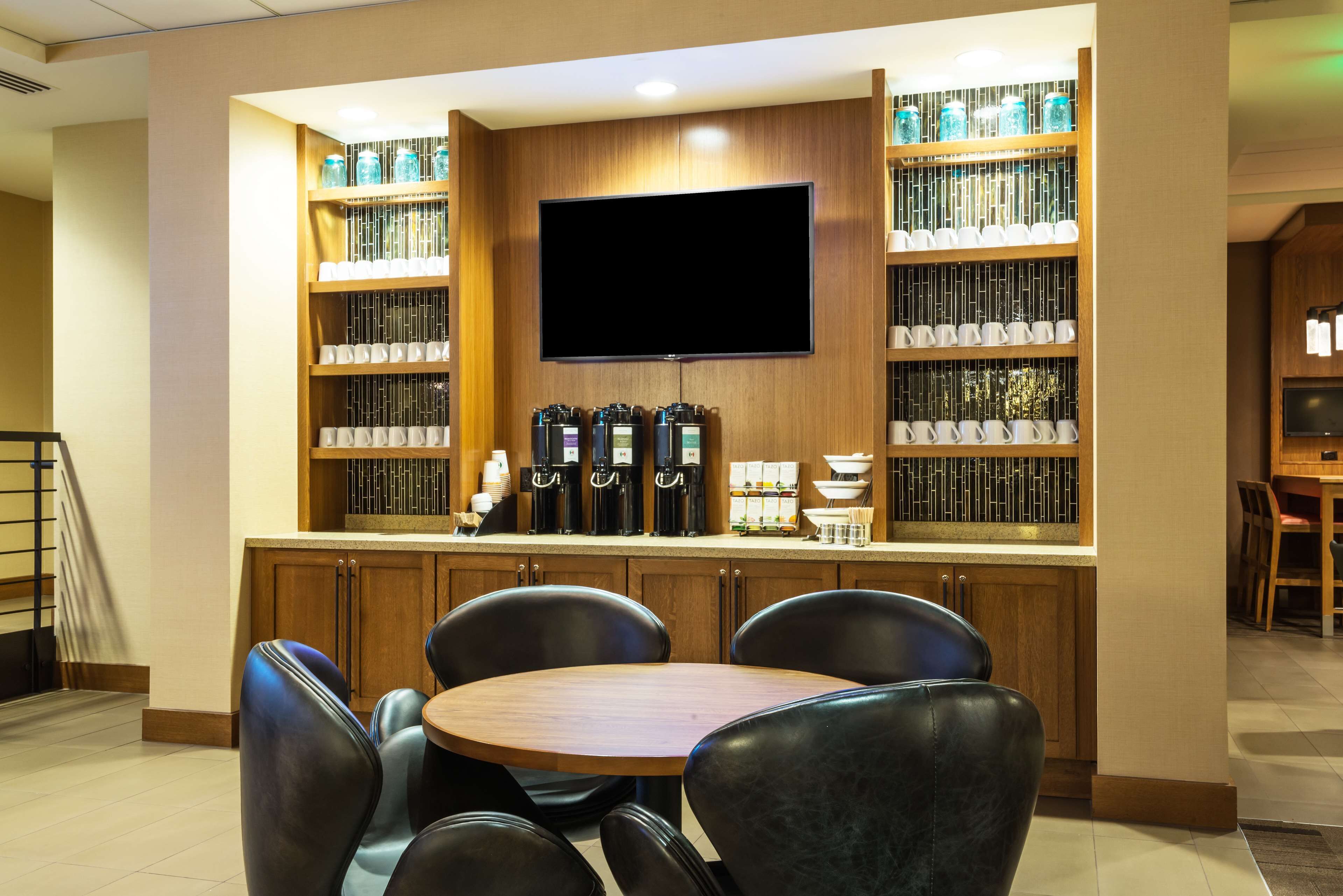 A modern bar area with a flat-screen TV, shelves of glassware, and coffee machines.