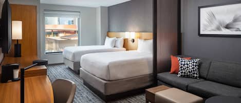 A hotel room with two beds, a sofa, a desk, and a view of the city.
