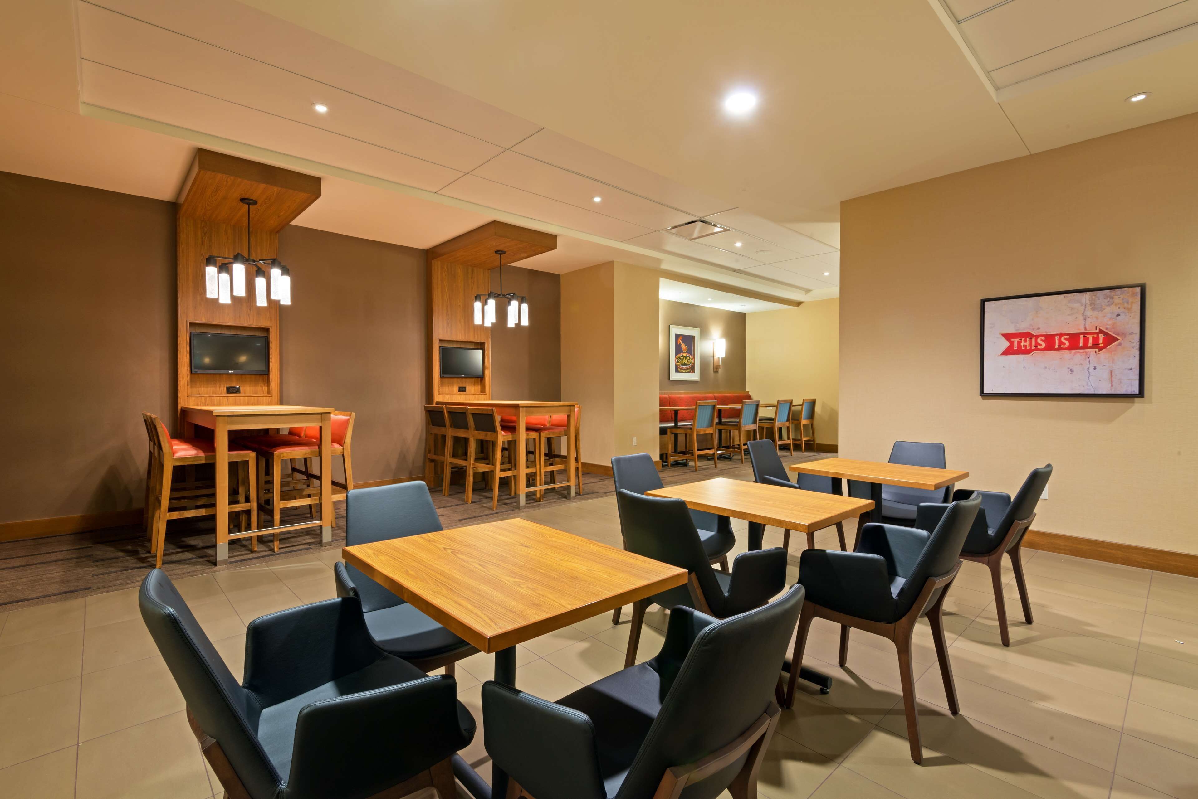 A hotel room with a wooden desk, chairs, a flat-screen TV, and a wall-mounted artwork.