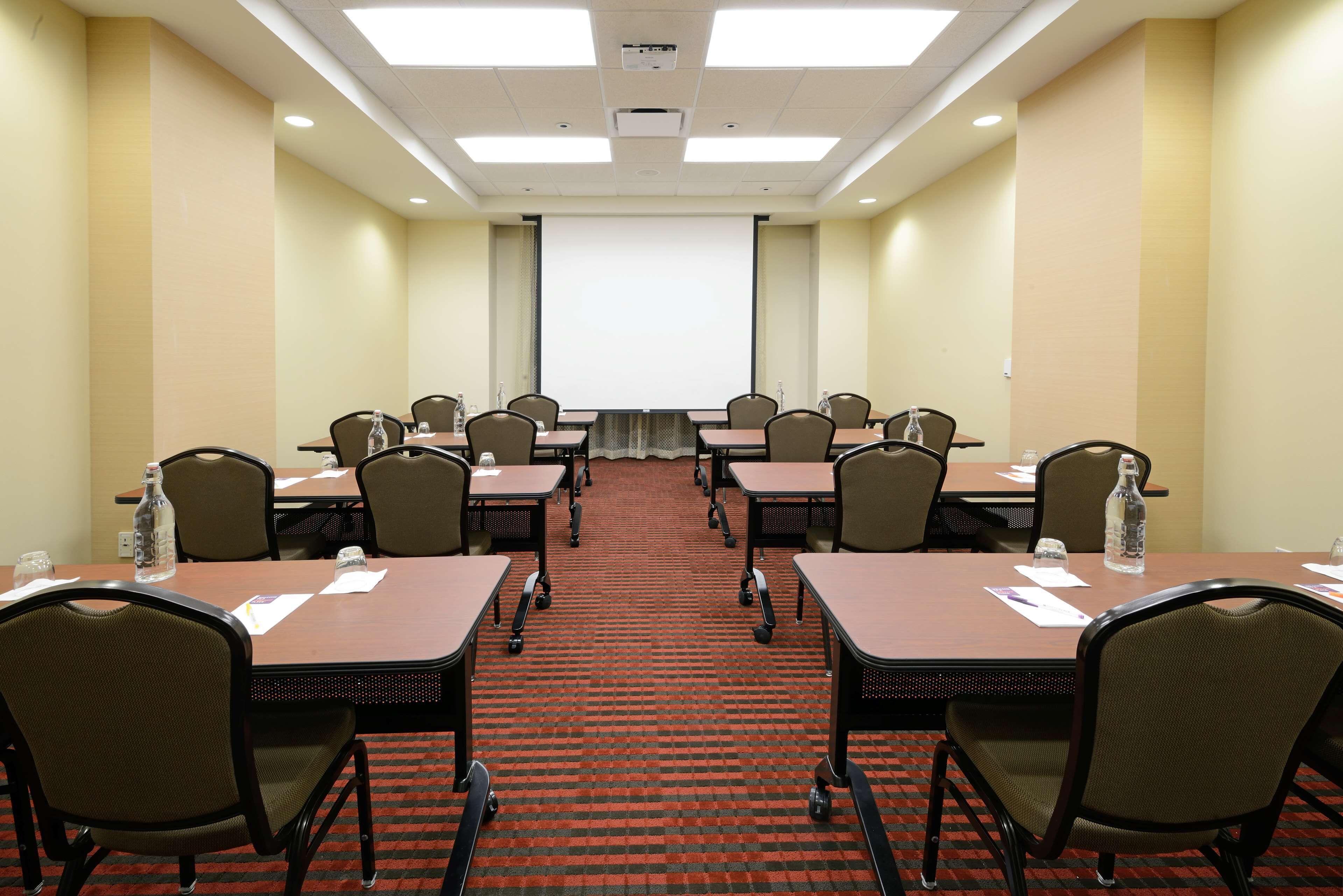 A conference room with a large screen, multiple tables, and chairs.
