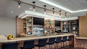 Een moderne bar met een lange toonbank, meerdere barkrukken en een televisiescherm.