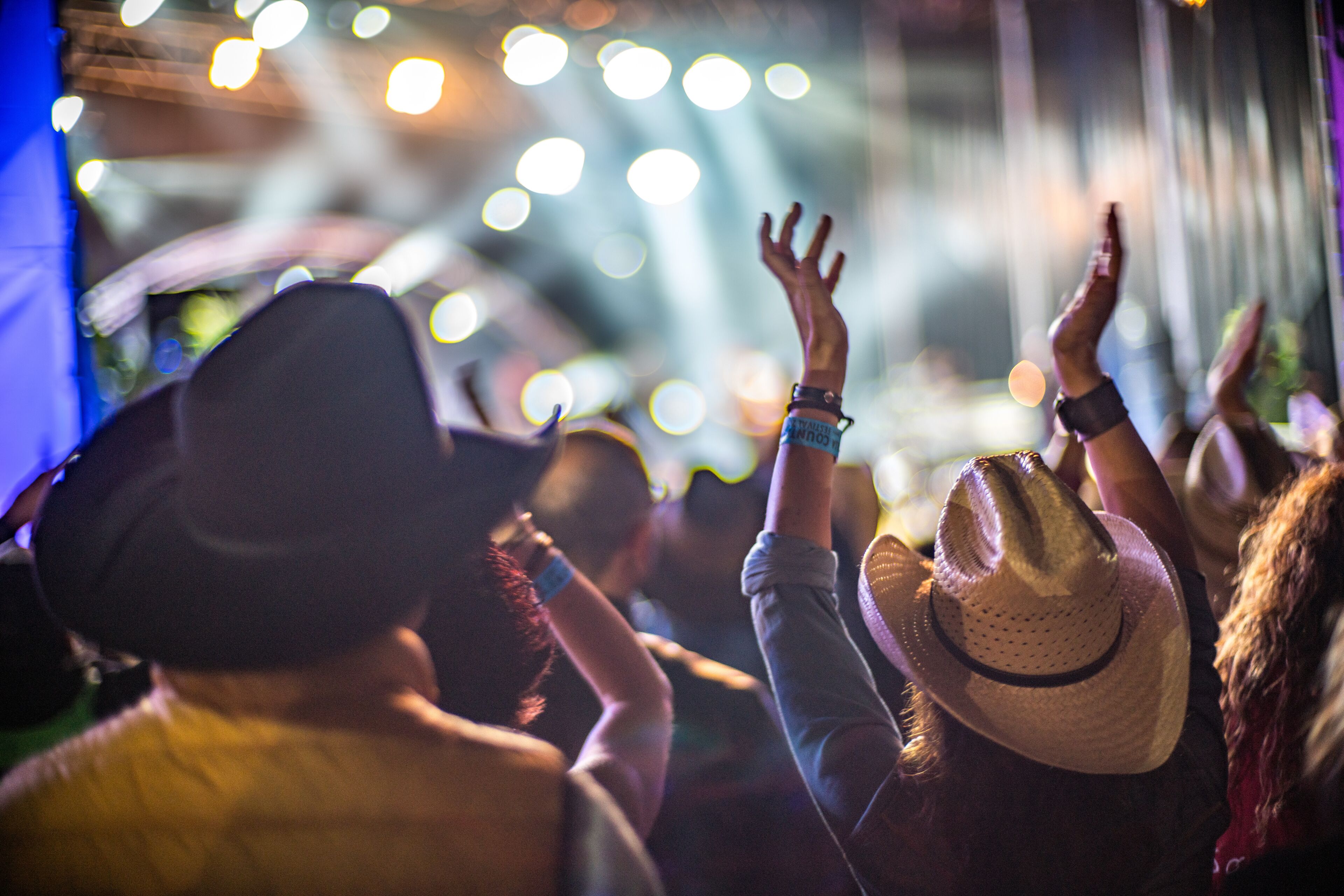 A crowd of people at an event with raised hands, some wearing hats.
