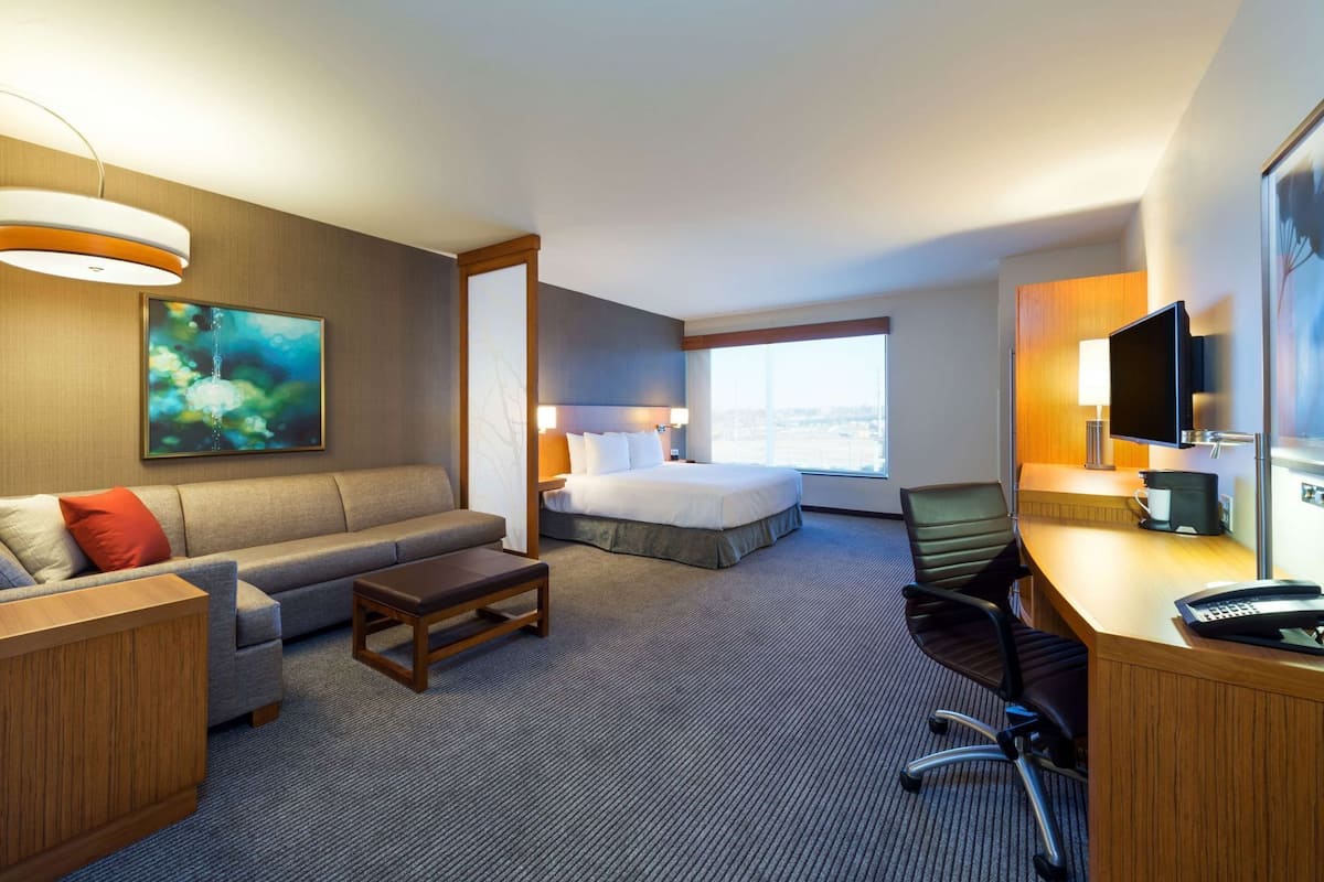 Una habitación de hotel con cama, sofá, escritorio y un ventanal grande.