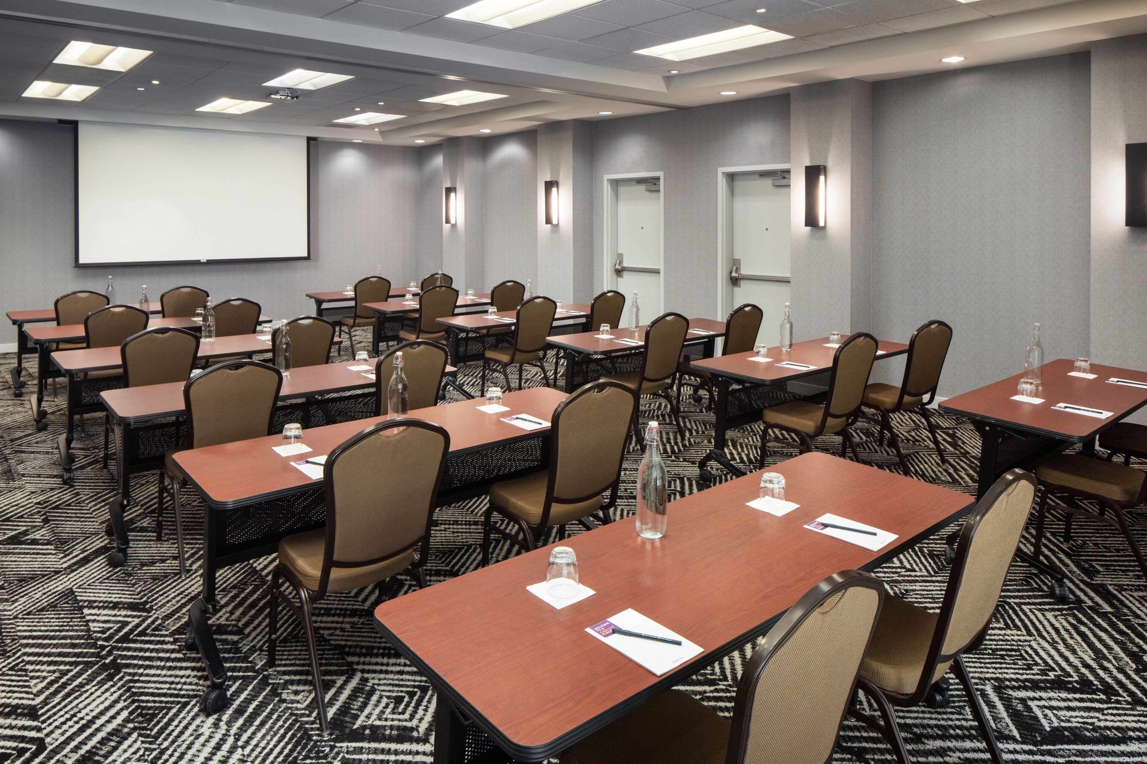A conference room with multiple tables and chairs, equipped with water bottles and notepads.