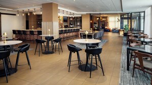 Een moderne hotelentree met een bar, diverse zithoeken en een groot televisiescherm.