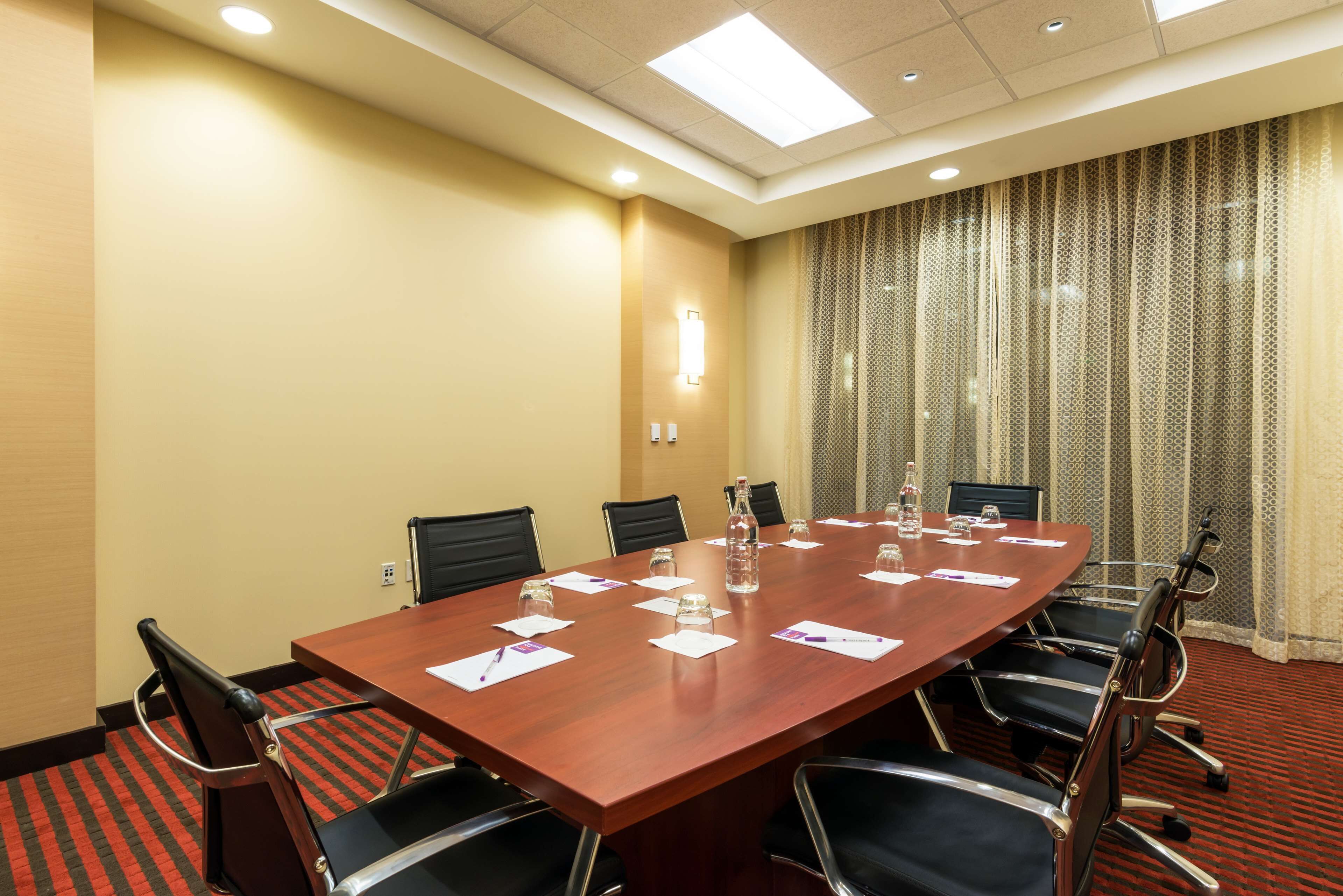 A conference room with a long wooden table, black chairs, and a red carpeted floor.