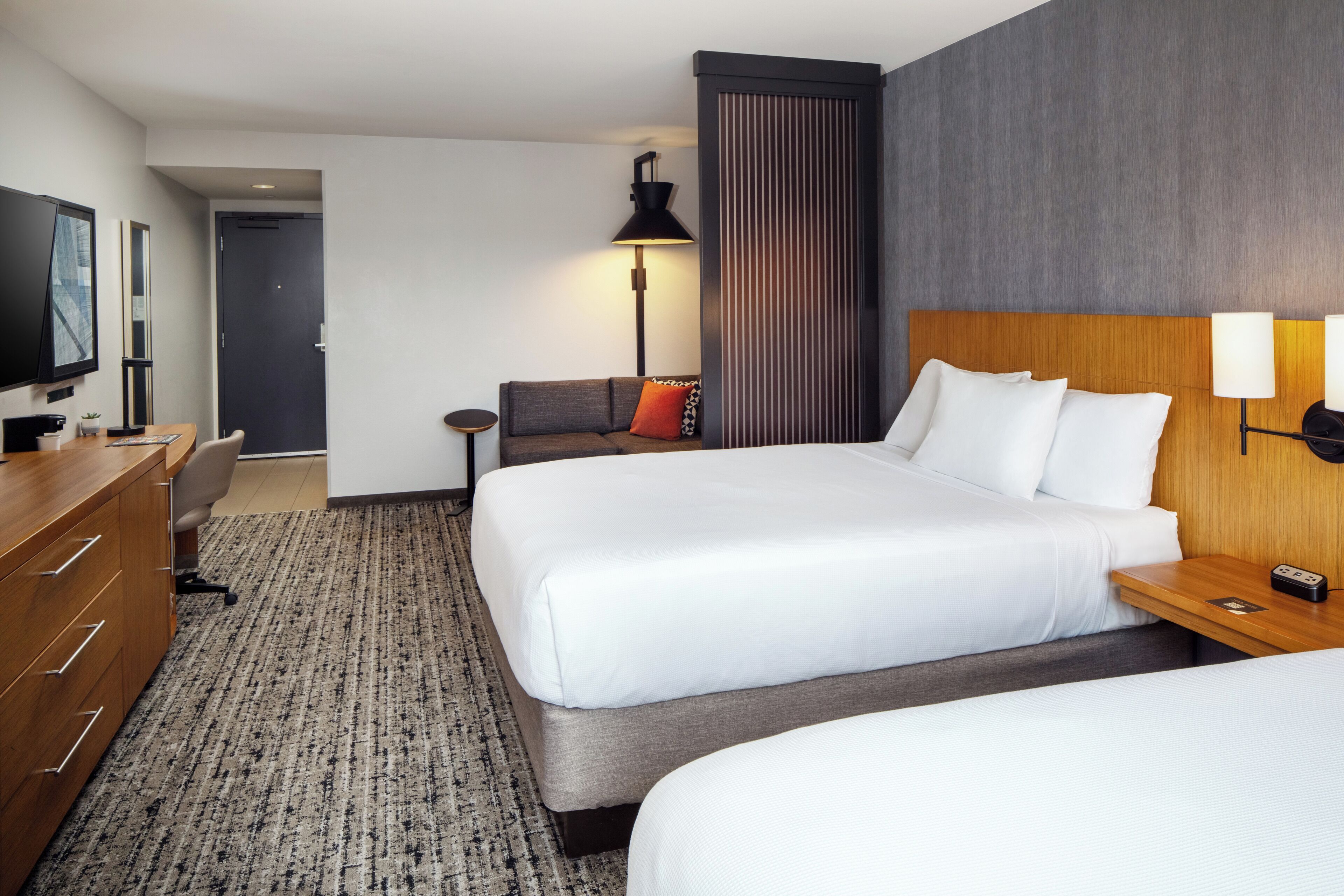 A hotel room with two beds, a desk, a TV, and a lamp.