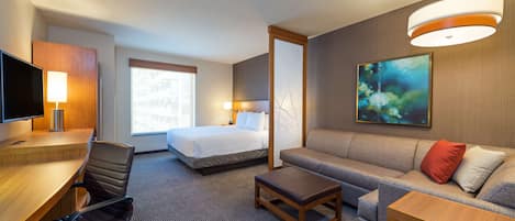 A hotel room with a bed, a sofa, a desk with a chair, a TV, and a painting on the wall.