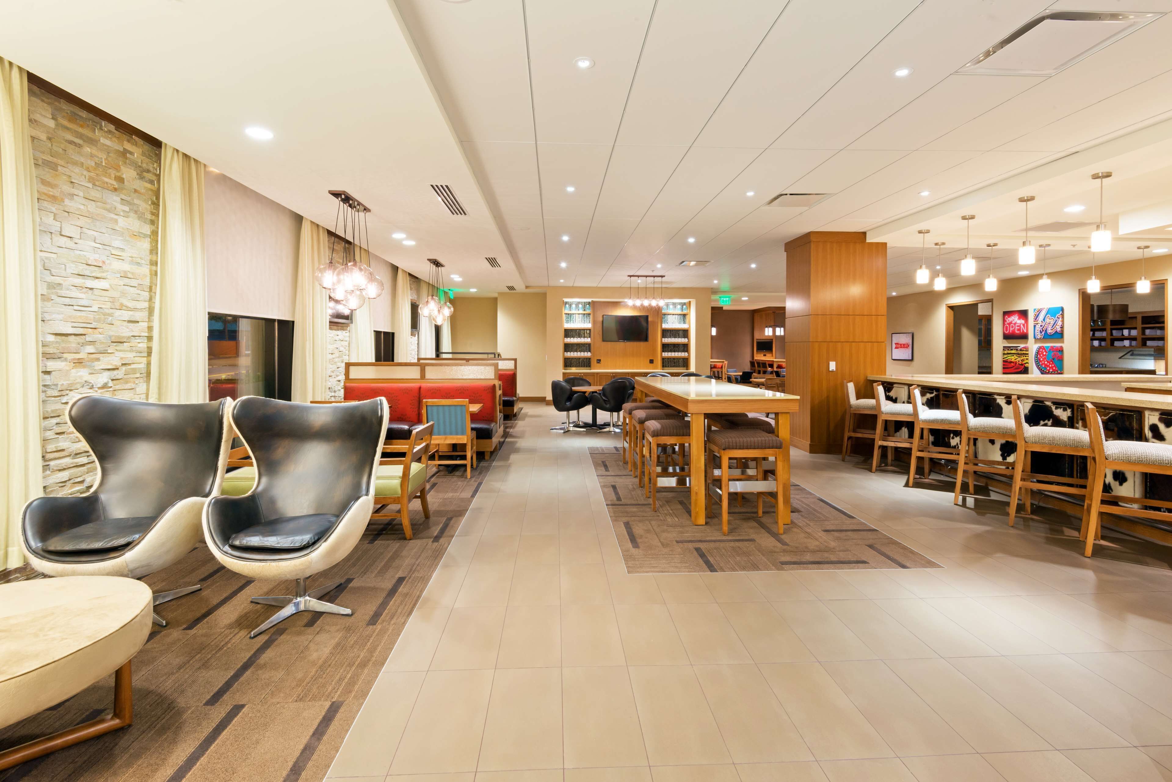 A modern hotel lobby with a central seating area, a bar, and a TV screen.
