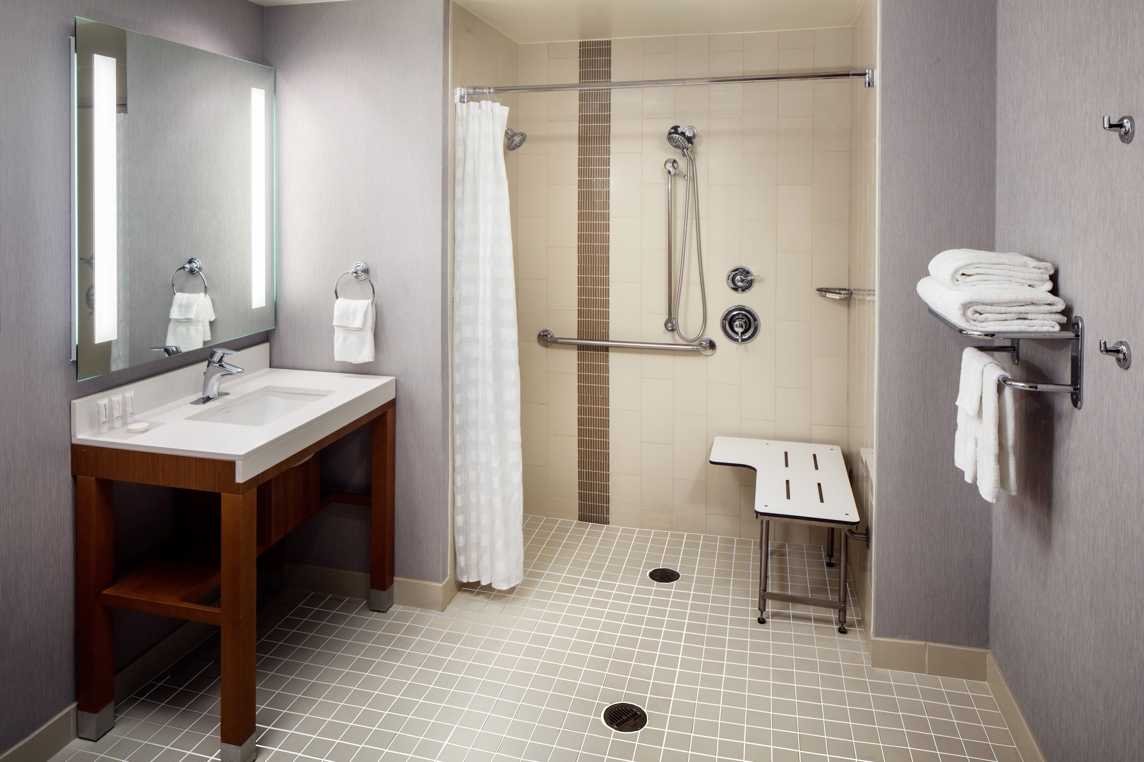 Un baño moderno con lavamanos, espejo, ducha y toallero.