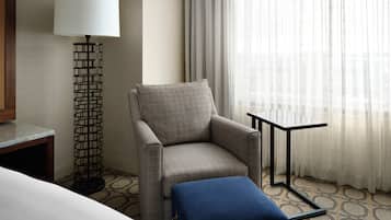 A hotel room with a checkered armchair, a small table, a lamp, and a window with sheer curtains.