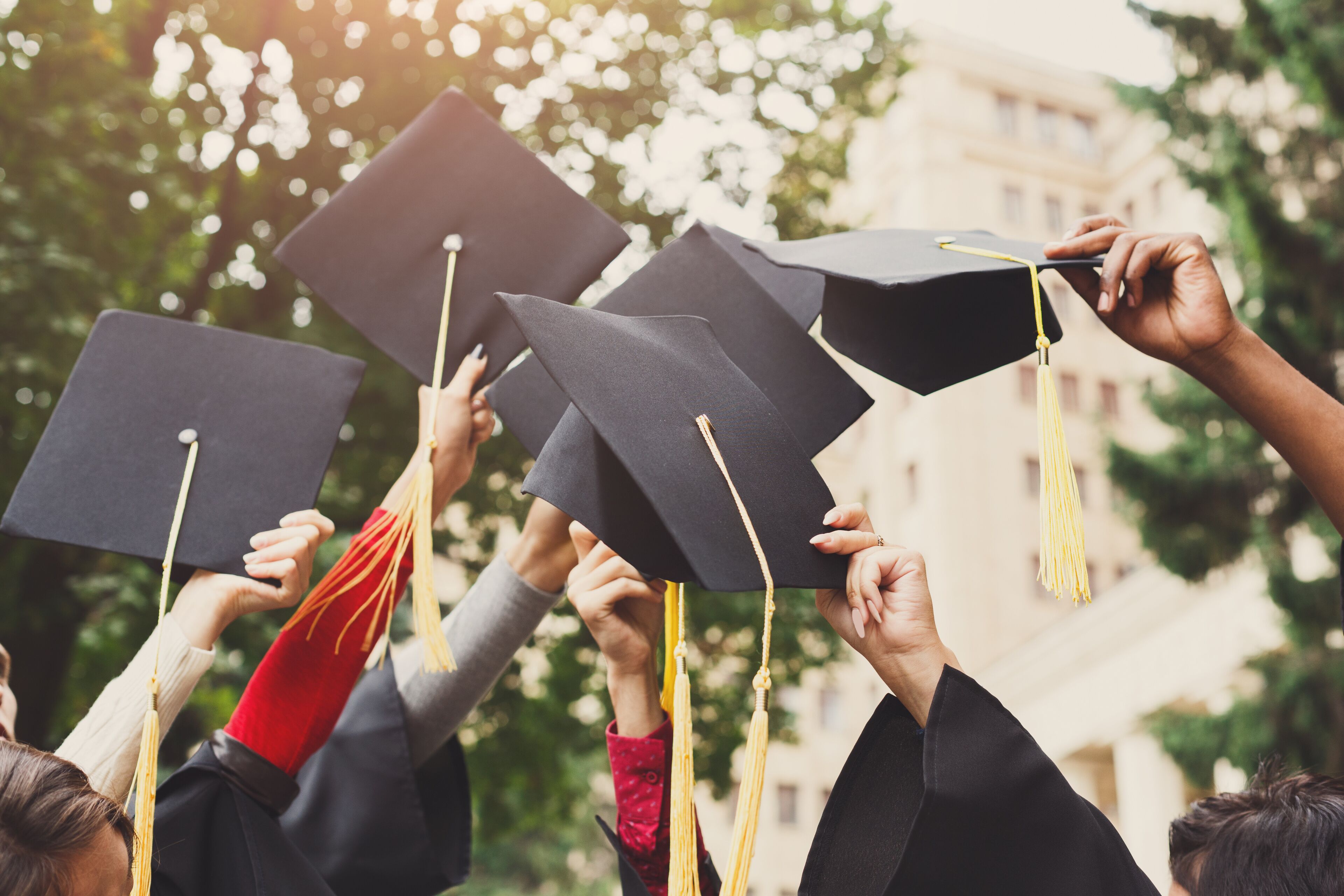 A group of people wearing graduation caps and gowns, holding their caps up in the air.