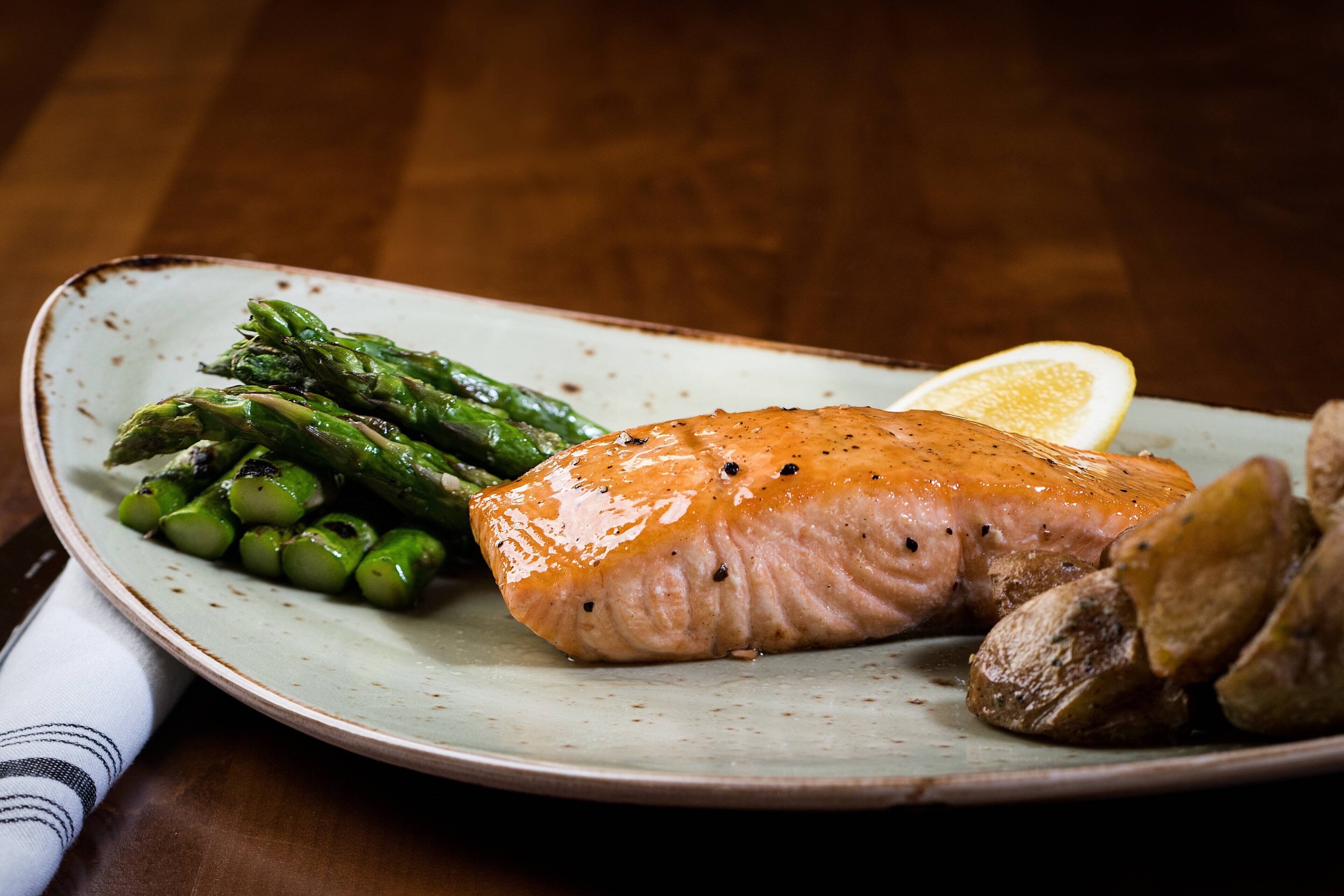 Een bord met gegrilde zalm, asperges en partjes citroen.