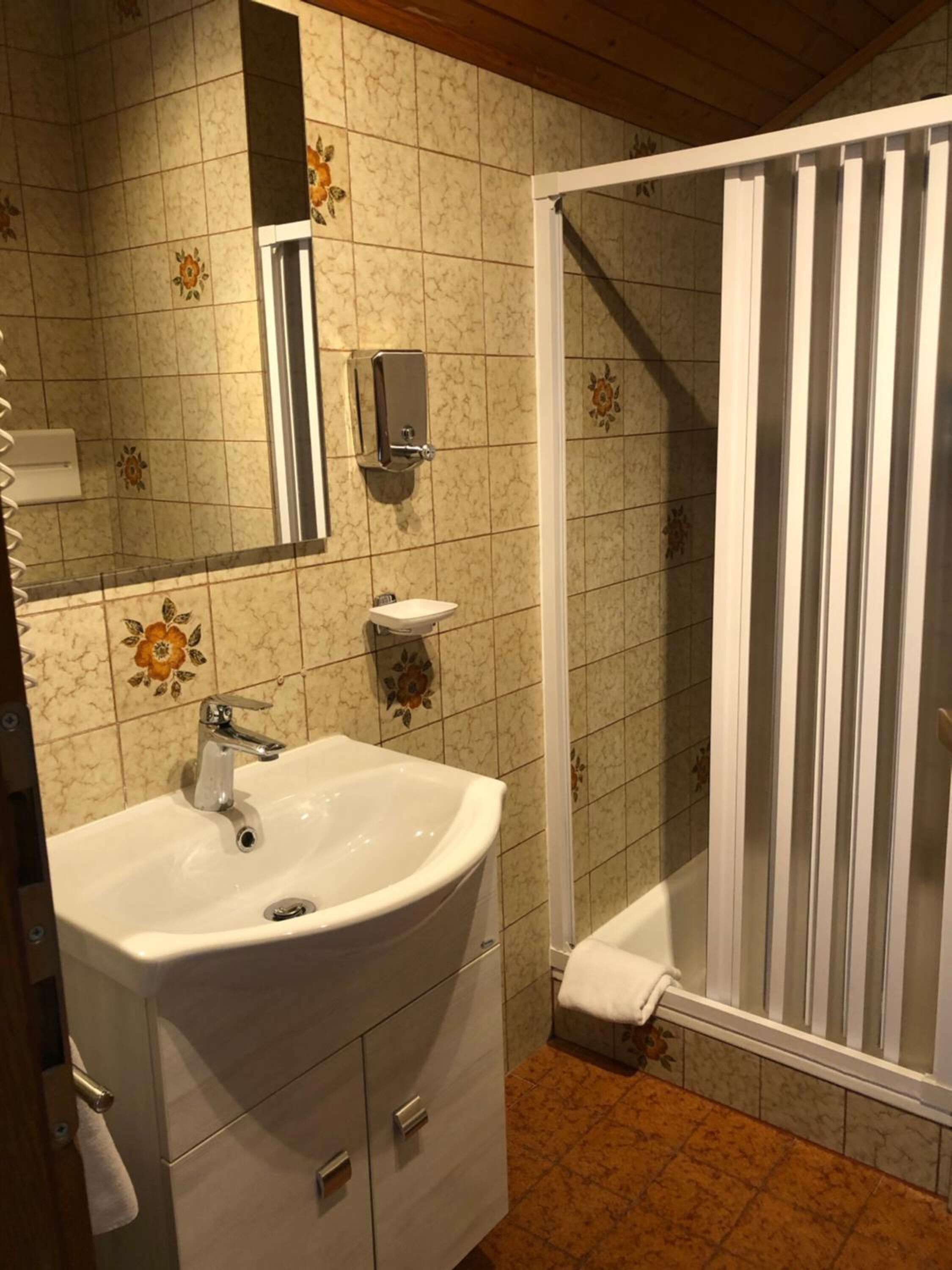 Une salle de bain avec un lavabo blanc, un miroir et une douche équipée de barres verticales.