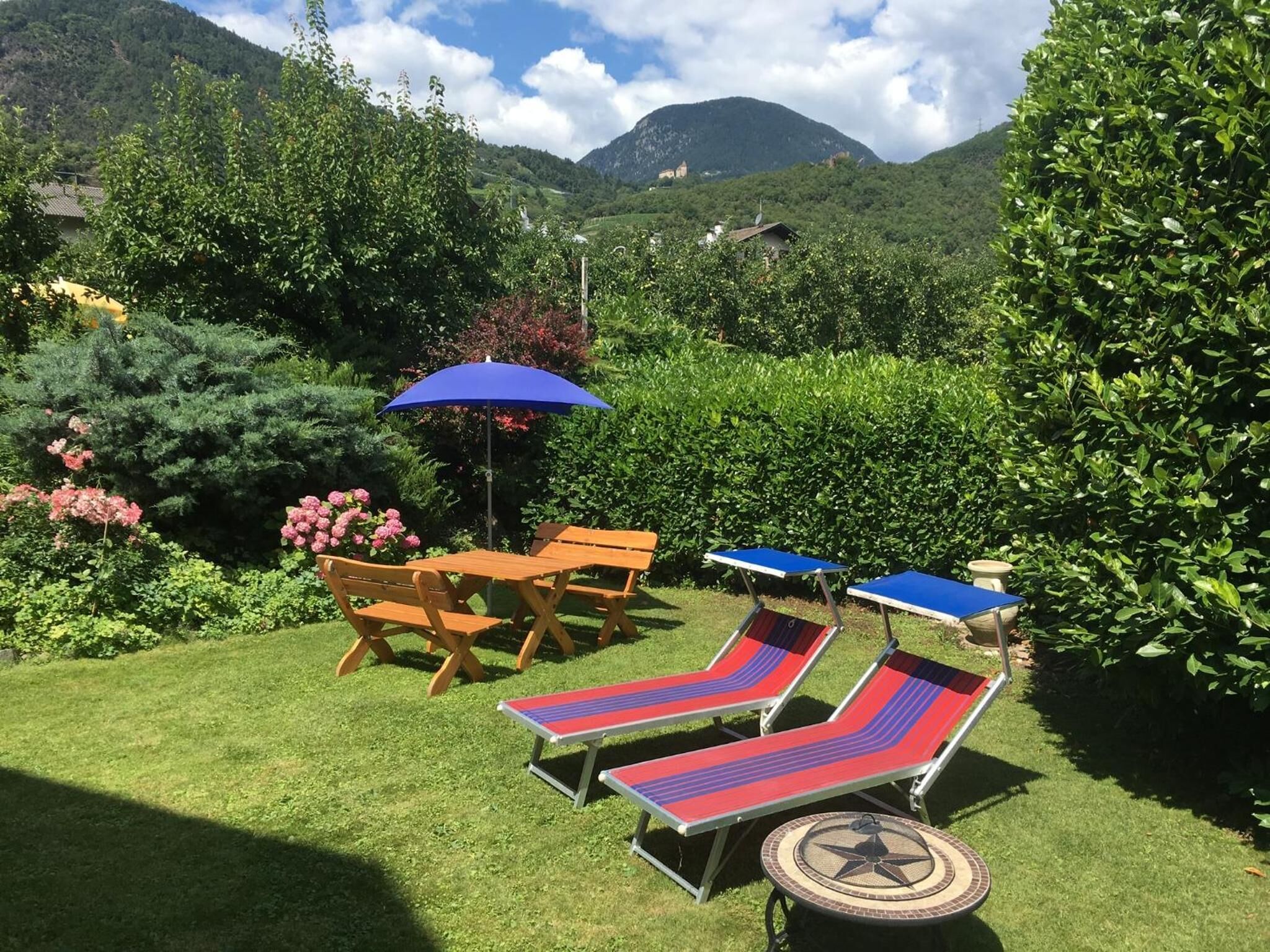 Un jardin avec une table et des chaises, deux fauteuils de jardin et un parasol bleu.