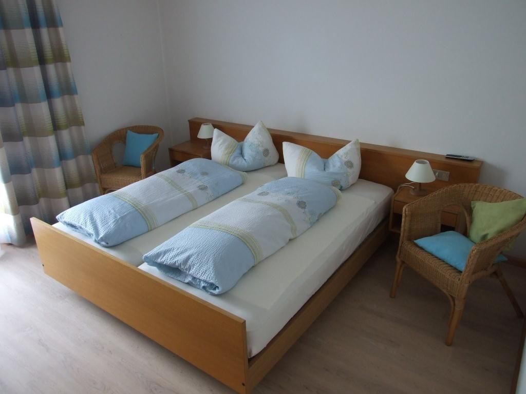 A double bed with a wooden frame, two nightstands, two wicker chairs, and a lamp.