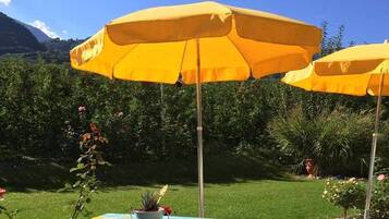A garden with yellow umbrellas, a grassy area, and a mountain in the background.