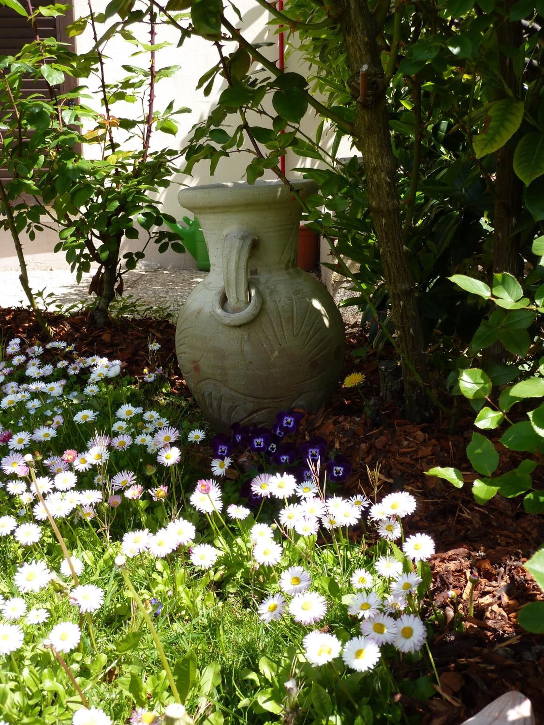 A garden with a large vase, surrounded by white and purple flowers.
