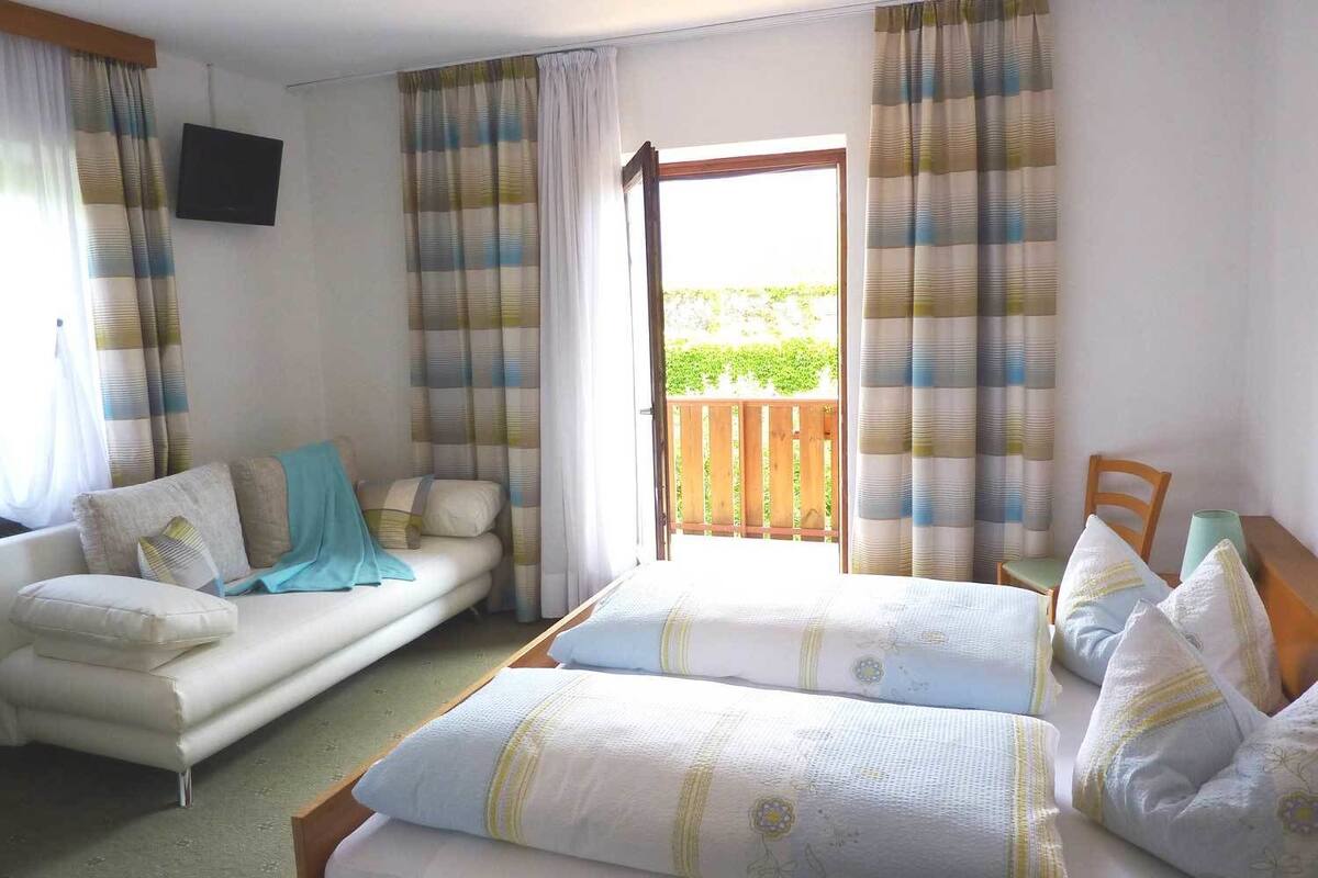 A bedroom with a double bed, a sofa, a TV, and a balcony with curtains.