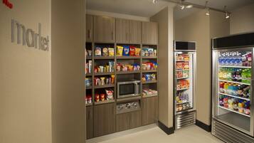 Una kitchenette con microondas, estantes llenos de aperitivos y un refrigerador con bebidas.