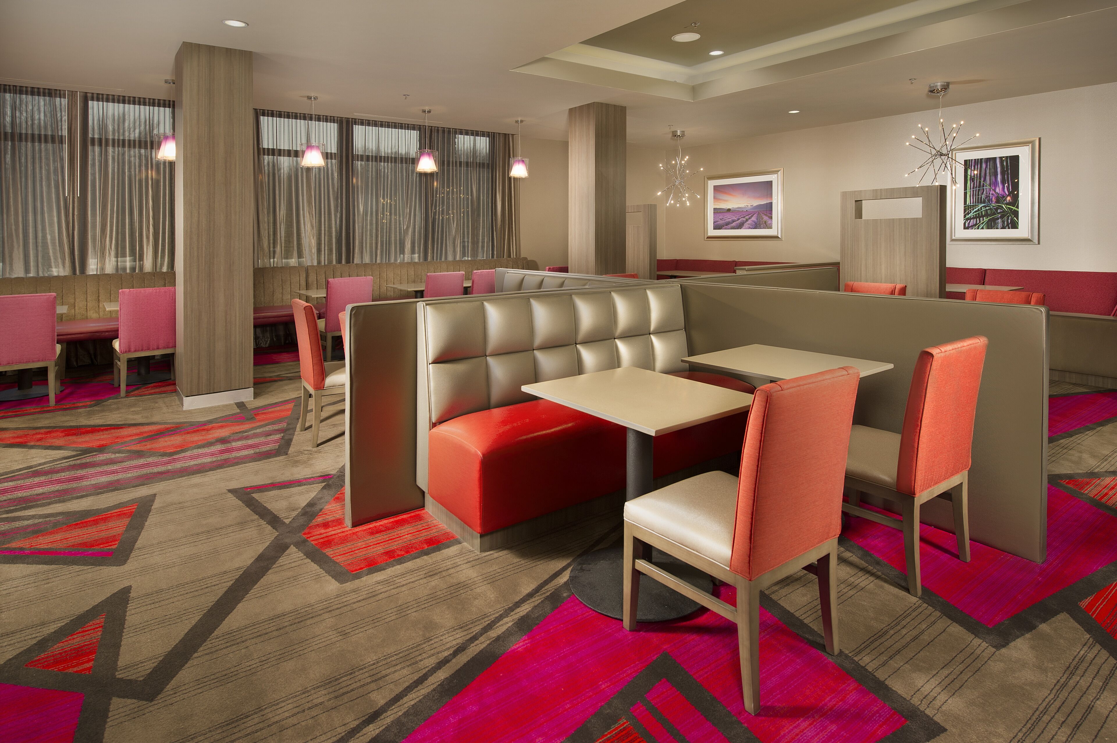 A modern hotel lobby with seating areas, including booths and tables, and a carpeted floor.